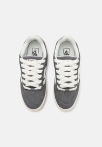 Baskets en daim gris avec des lacets blancs, présentant une tige texturée, des perforations sur le bout et une semelle en caoutchouc de couleur crème.