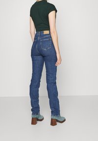 Jeans de mezclilla azul de talle alto con una silueta ajustada, costuras en contraste y un parche de cuero marrón en la cintura trasera.