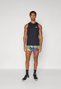 Camisola preta sem mangas, calções com padrão multicolorido, sapatos desportivos pretos e meias escuras. Design simples e contrastes de cores vibrantes.