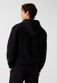 Sweat à capuche noir avec ourlet et poignets côtelés. Confectionné en tissu doux et texturé. Comprend une poche kangourou et une coupe décontractée.