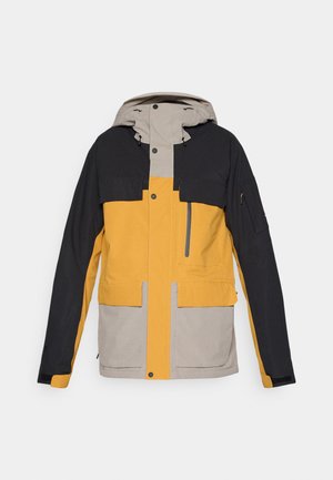 Színblokkolt dzseki fekete, sárga és bézs színű szakaszokkal. Kapucnival, több zsebbel és cipzáras mellzsebbel rendelkezik. Vízálló anyagból készült.