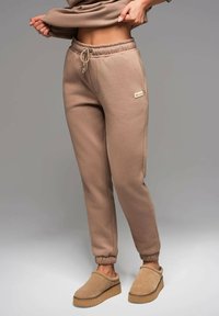 Beige joggers i mjukt tyg, med resårmidja och dragsko, muddade avslut och sidofickor. Tillsammans med beige slip-on skor.