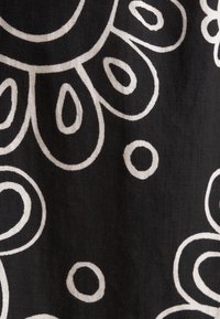 Schwarzer Stoff mit weißen, abstrakten Blumen- und kreisförmigen Mustern, einer strukturierten Oberfläche und einem fließenden Design.
