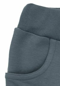 Szare spodnie dresowe z prążkowanym pasem i boczną kieszenią. Miękka, gładka tekstura, prosty design bez widocznych wzorów ani zdobień.