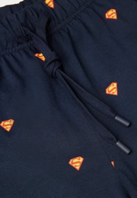 Marina blå shorts med dragsko i midjan, prydda med spridda mönster av röda och gula Superman-logotyper. Tillverkade av mjukt, slätt tyg.
