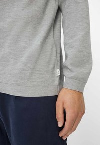 Hellegrauer Strickpullover mit strukturiertem Muster, gerippten Bündchen und Saum. Verfügt über ein kleines Markenetikett auf der linken Seite, nahe dem Boden.