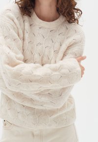 Krämfärgad stickad jumper med ett strukturerat mönster av sammanlänkade ovala former, avspänt snitt, vida ärmar och ribbad halsringning.