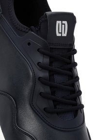 Marineblauwe leren sneaker met textuur, zwarte veters en een prominent logo op de tong. Rond neuwwerk en witte zool.