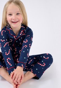 Conjunto de pijama azul marino con patrones de bastones de caramelo y corazones, con ribetes rojos en el cuello y los puños, hecho de tela suave.