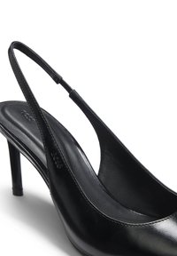 Μαύρο δερμάτινο γόβα με λουράκι στο πίσω μέρος, μυτερή μύτη και λεπτό τακούνι στιλέτο, με ορατό ανάγλυφο λογότυπο στη λουρίδα και στην εσωτερική σόλα.