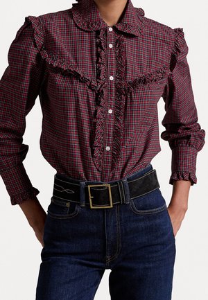 Rød og sort ternet bluse med lange ærmer og flæser langs fronten og skuldrene, kombineret med mørkeblå jeans og et sort bælte med en guldbøjle.