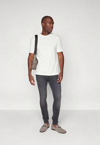 T-shirt branca de manga curta combinada com jeans cinza escuro de corte slim e mocassins cinzentos. Uma pequena bolsa cinza de tiracolo é usada ao ombro.