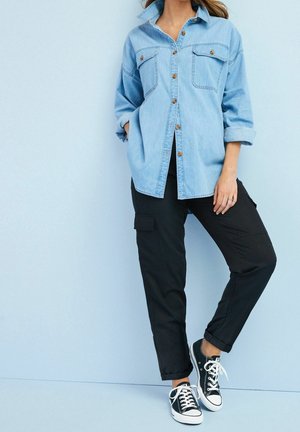 Světlomodrá džínová košile s knoflíkovým zapínáním vpředu a dvěma kapsami na prsou, doplněná o černé cargo kalhoty a černé tenisky z plátna.