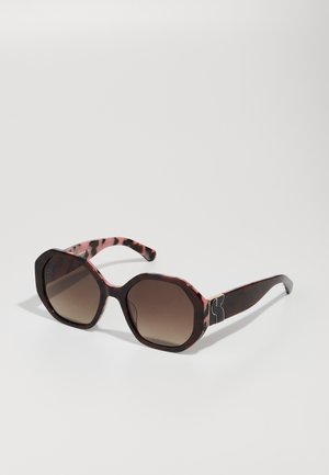 Lunettes de soleil octogonales en écaille marron foncé avec des verres dégradés marron. Présente des accents en doré sur les branches. Finition texturée.