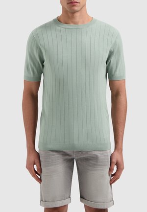 Lichtgroene gebreide trui met korte mouwen en verticale ribbelstructuur, ronde ronde hals en aansluitende taille, gecombineerd met grijze shorts met opgerolde manchetten.