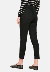 Pantalones elásticos negros de corte ajustado, con un detalle de cremallera en el tobillo y bolsillos. Combinados con una blusa a rayas en blanco y negro y zapatos planos con tachuelas.