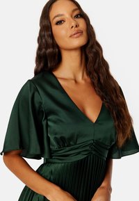 Robe en satin vert avec un décolleté en V, des manches courtes à volants et une jupe plissée pour la texture ; finition en tissu lisse et silhouette élégante.