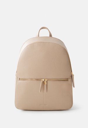 Sac à dos beige texturé avec poche zippée devant, tirettes de fermeture éclair dorées et poignée supérieure, présenté sur un fond clair uni.