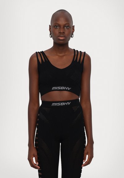 Top noir court avec plusieurs fines bretelles. Associé à un legging noir taille haute avec des découpes et un motif texturé. Logo de la marque visible.