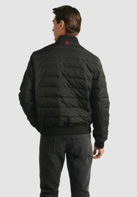 Czarna kurtka puchowa ma pikowany design, ribbowe mankiety i kołnierz. Małe logo widoczne jest na tylnej części dekoltu.