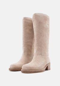 Bottes mi-mollet en daim beige avec bouts arrondis, talons empilés en bois et détails de couture subtils sur fond blanc.