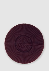 Berretto lavorato a maglia bordeaux con texture a coste, forma circolare e un dettaglio centrale con un motivo in rilievo. Materiale morbido in misto lana.