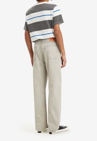 Grå och vit randig kortärmad skjorta i kombination med ljusgrå raka jeans och svarta sneakers; synlig märkesetikett på jeansen.