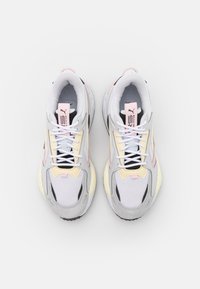 Atletické tenisky s vrchní částí z mřížkované tkaniny a semiše v bílé, šedé a jemných pastelových barvách, s tlustou podrážkou a kontrastními černými akcenty.