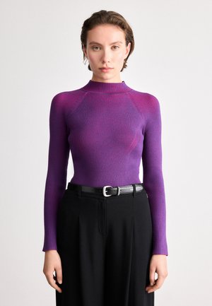 Top lungo a maniche lunghe viola a coste con collo alto e forma aderente, abbinato a pantaloni neri a vita alta e una cintura nera.