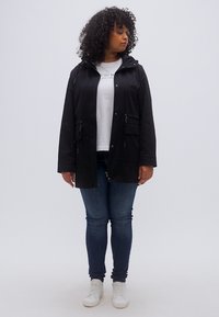 Μαύρο ελαφρύ μπουφάν με κουκούλα, εμπρόσθιο φερμουάρ και κουμπιά, σούρα στη μέση και δύο πλαϊνές τσέπες, που φοριέται πάνω από λευκό πουκάμισο και τζιν παντελόνι.