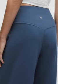 Marina blå yogabyxor med bred midjeband, tillverkade av mjukt, stretchigt material; har subtila sömmar och en logo på baksidan.