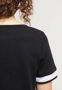 T-shirt nera con maniche corte e dettagli in rete bianca. Il girocollo è semplice e arrotondato, evidenziando una texture liscia.