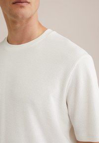 Camiseta blanca de manga corta confeccionada en tejido de punto waffle texturizado, con cuello redondo y un ajuste relajado.