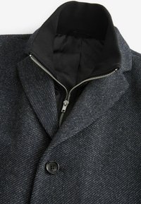 Mörkgrå kappa i ullblandning med dragkedja fram, stor krage och textil med struktur samt svart innerfoder. Svart knapprad fram.