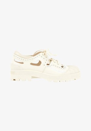 Chaussure en cuir blanc à coupe basse avec détails découpés, laçage à l'avant, semelle épaisse crantée et nom de la marque embossé sur le talon.