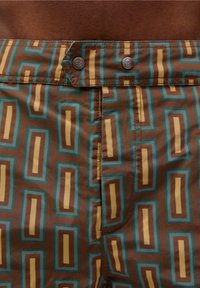 Bruine shorts met een geometrisch patroon van blauwe en gele rechthoeken, voorzien van metalen drukknoopjes en zichtbare stiksels.