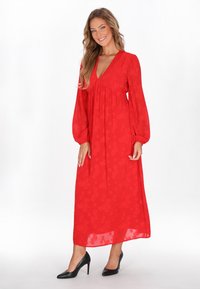Punainen maksi mekko, jossa on pitkät, puffatut hihat, V-pääntie ja kukkatekstuuri; yhdistetty mustiin korkokenkiin. S sileä kangas.