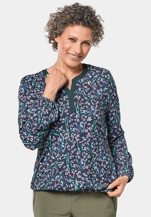 Langarmp blouse in marineblauwe stof met een bloemmotief in wit en teal. Voorzien van een V-hals met donkergroene rand en geplooide mouwen.