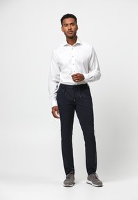 Witte langwerpige mouwen shirt met gouden knopen, gecombineerd met marineblauwe broek met een trekkoord in de taille, en grijze sneakers met een gestructureerde afwerking.