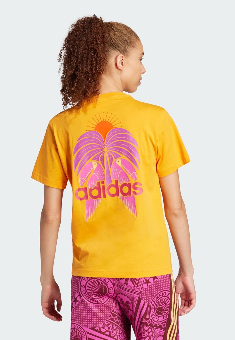 Žluté bavlněné tričko s potiskem palmy a tukana, s růžovými akcenty a tučným nápisem "adidas" na zadní straně.
