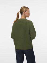 Pulôver verde de malha com um corte descontraído, bainha canelada e gola redonda. O tecido parece suave e texturizado, complementando uns jeans de ganga escura.
