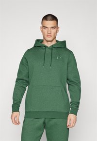 Felpa con cappuccio verde realizzata in tessuto texturizzato, dotata di tasca frontale e un piccolo logo sul petto. Il design include un cappuccio regolabile con cordoncino.