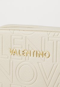 Bežna teksturirana usna torbica s utisnutim slovima i zlatnim hardverom na kojem je prikazano ime branda "Valentino."