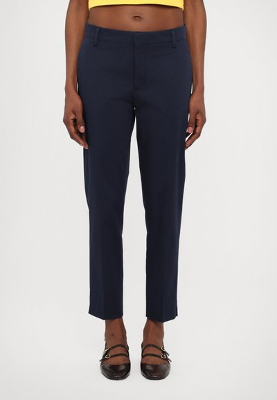 Marineblau gefütterte Hose mit geradem Schnitt, schrägen Fronttaschen und glatter Textur. Verkürzte Länge, kombiniert mit braunen Ballerinas.