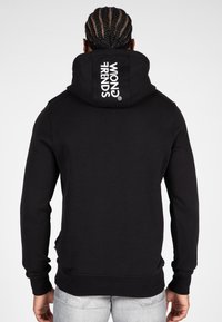 Zwarte hoodie van zachte stof met een groot, opvallend logo "WRONG TRENDS" op de achterkant, voorzien van een trekkoordkap en geribbelde manchetten.