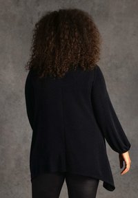 Top negro de manga larga con un corte relajado, que presenta un dobladillo curvado y una tela texturizada. Modelo mostrado de espaldas contra un fondo neutral.