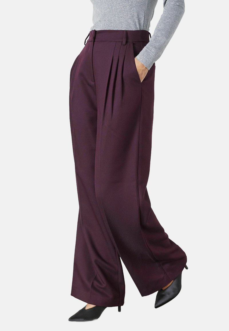 Hoge paarse broek met een textuurpatroon, plooien en zijzakken; gecombineerd met zwarte hakken en een aansluitend zilveren top.