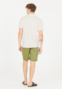 Vit polo skjorta, gröna shorts, bruna sandaler. Kortärmad polo med krage; shortsen är knälånga med uppvikta manschetter. Avslappnad look.