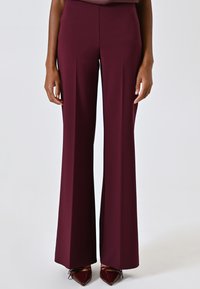 Pantalons à jambes larges en bordeaux foncé, fabriqués à partir d'un tissu lisse. Présentent une taille haute et un design minimaliste. Associés à des talons aiguilles rouge foncé.