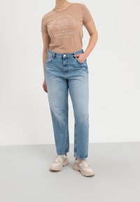 Béžové tričko s potiskem, světle modré džíny rovného střihu a béžové tenisky. Jednoduchý design a volný střih, s měkkou texturou.